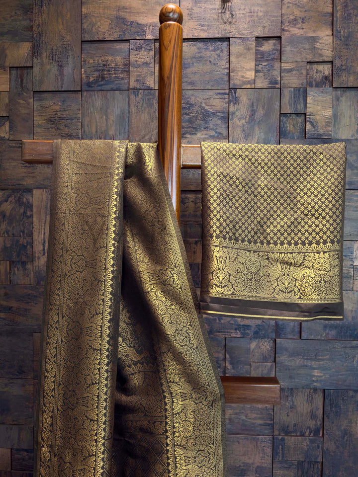 Two patterned towels hanging on a wooden towel rack against a wooden paneled wall. Art silk Black saree with dense gold zari jaal and traditional motifs displayed vertically. Authentic Indian ethnic wear featuring a striking black saree richly woven with golden threads, an exclusive House of Vardha design.