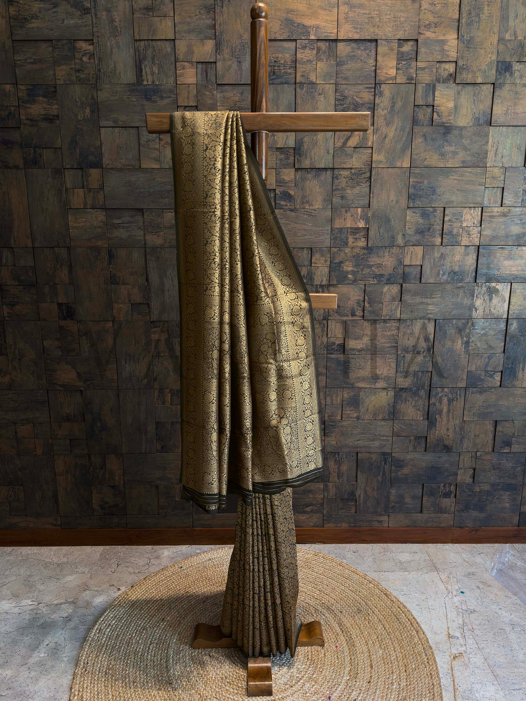 Black Mysore silk saree with golden zari weaving and traditional motifs displayed on a wooden stand.
