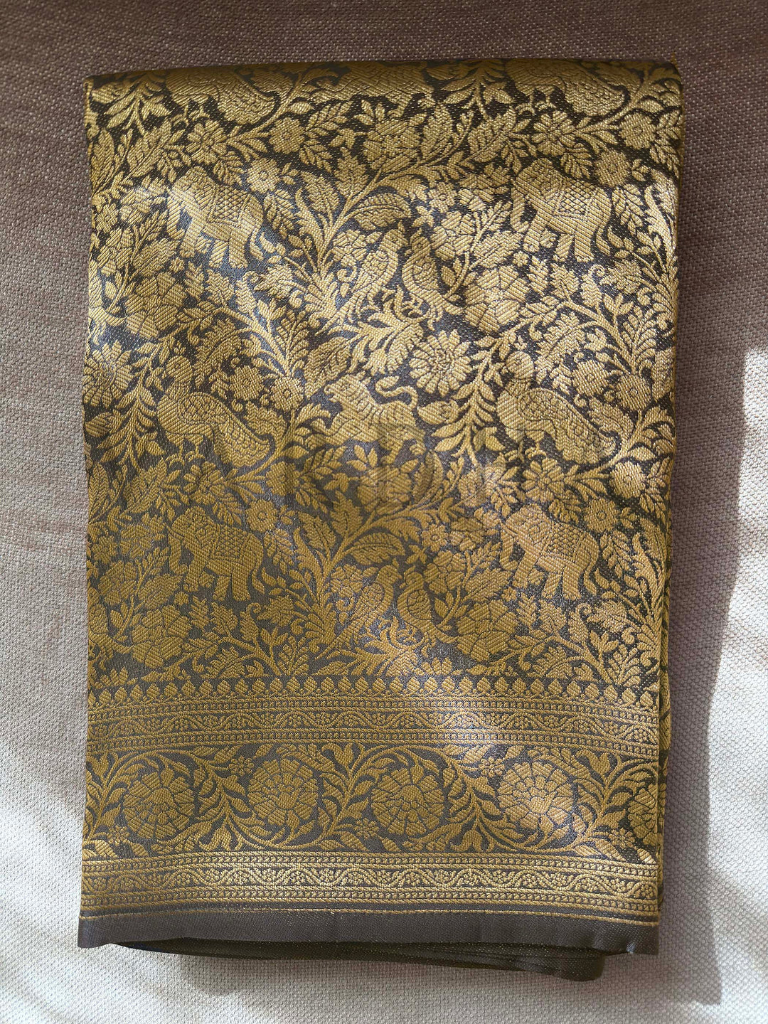 Decorative fabric with intricate gold and black pattern on a plain background  Folded black Mysore silk blouse piece with zari border and animal-floral motifs
