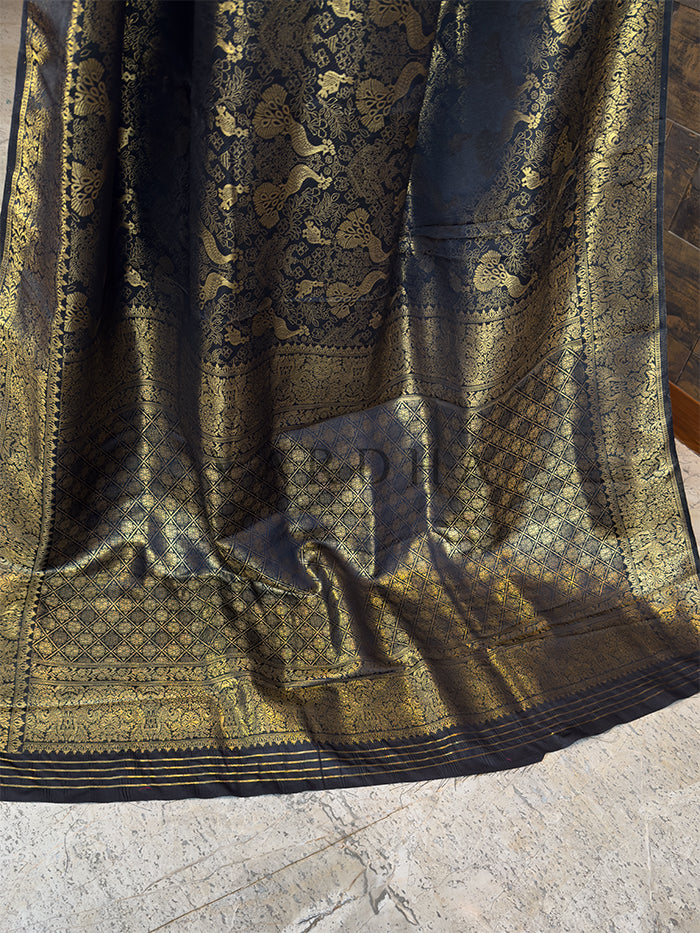 Decorative fabric with intricate patterns on a textured surface. Luxurious black Indian wedding saree from House of Vardha with all-over gold brocade work and a striking geometric patterned edge.