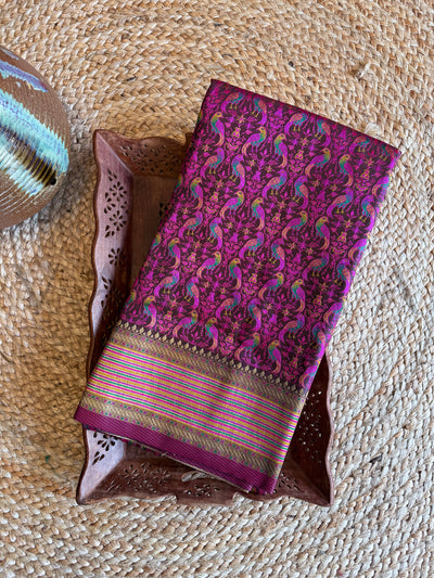 Folded black satin Tanchoi silk saree with colorful thread-woven parrot motifs and golden striped border, elegant for gifting or pooja