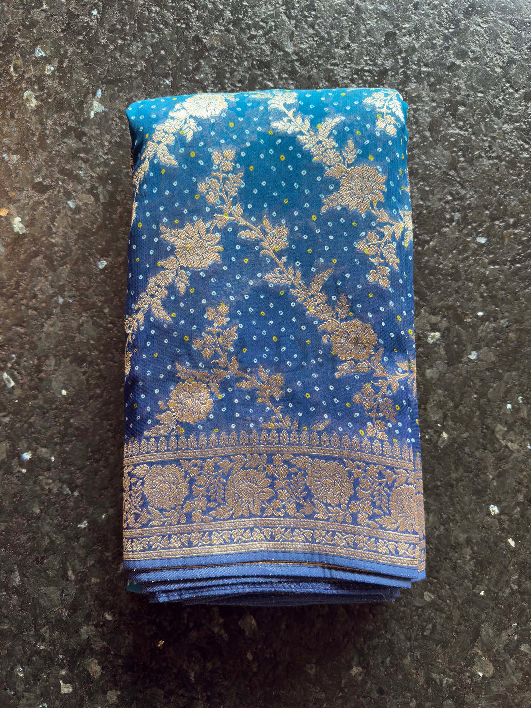 Folded blue fabric with gold patterns on a dark surface