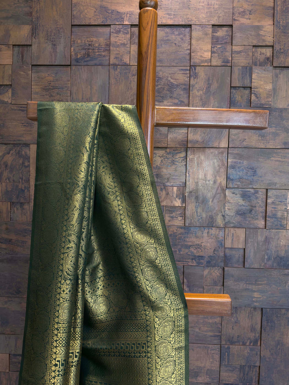 Close-up of border showing antique gold circular motifs on bottle green silk Green fabric draped over a wooden hanger against a wooden paneled wall.