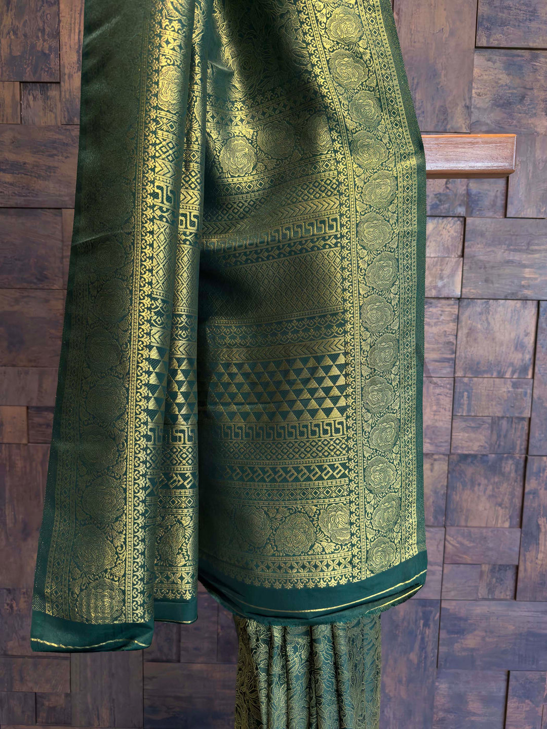 Green embroidered fabric draped over a wooden surface Full-body floral and geometric zari weaving on bottle green Kanjivaram fabric