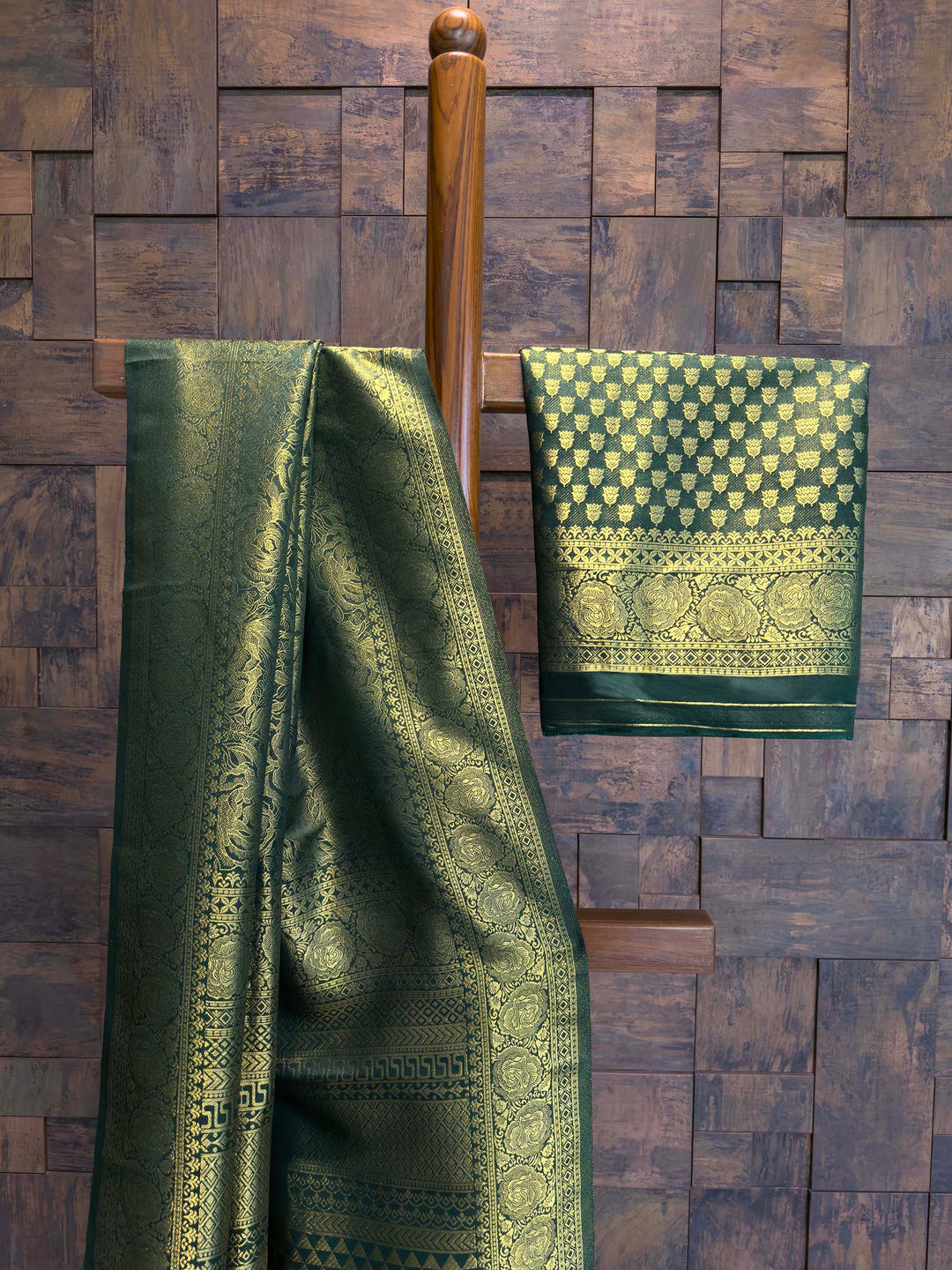 Green patterned fabric draped over a wooden rod against a wooden paneled wall. Bottle Green Antique Gold Zari Kanjivaram Silk Saree-794-