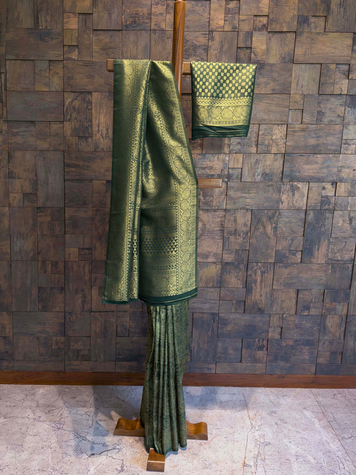 Green saree with a pattern on a wooden stand against a stone wall. Detailed close-up of antique gold zari craftsmanship on bottle green saree