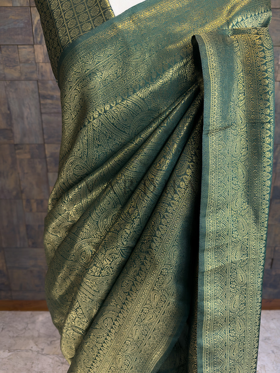 Close-up of House of Vardha Bottle Green Golden Zari Kanjivaram Silk Saree highlighting the exquisite geometric gold zari patterns on the pallu. Green saree with intricate patterns on a wooden floor