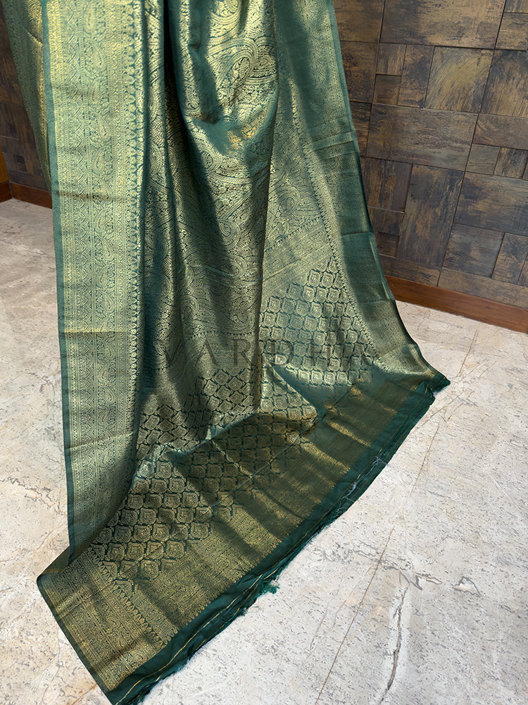 Luxurious authentic Kanjivaram Indian wedding saree in rich bottle green from House of Vardha with extensive gold brocade. Green embroidered fabric draped over a wooden surface