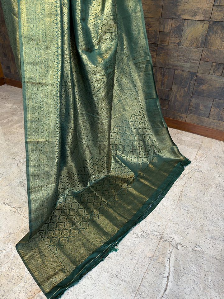 Luxurious authentic Kanjivaram Indian wedding saree in rich bottle green from House of Vardha with extensive gold brocade. Green embroidered fabric draped over a wooden surface