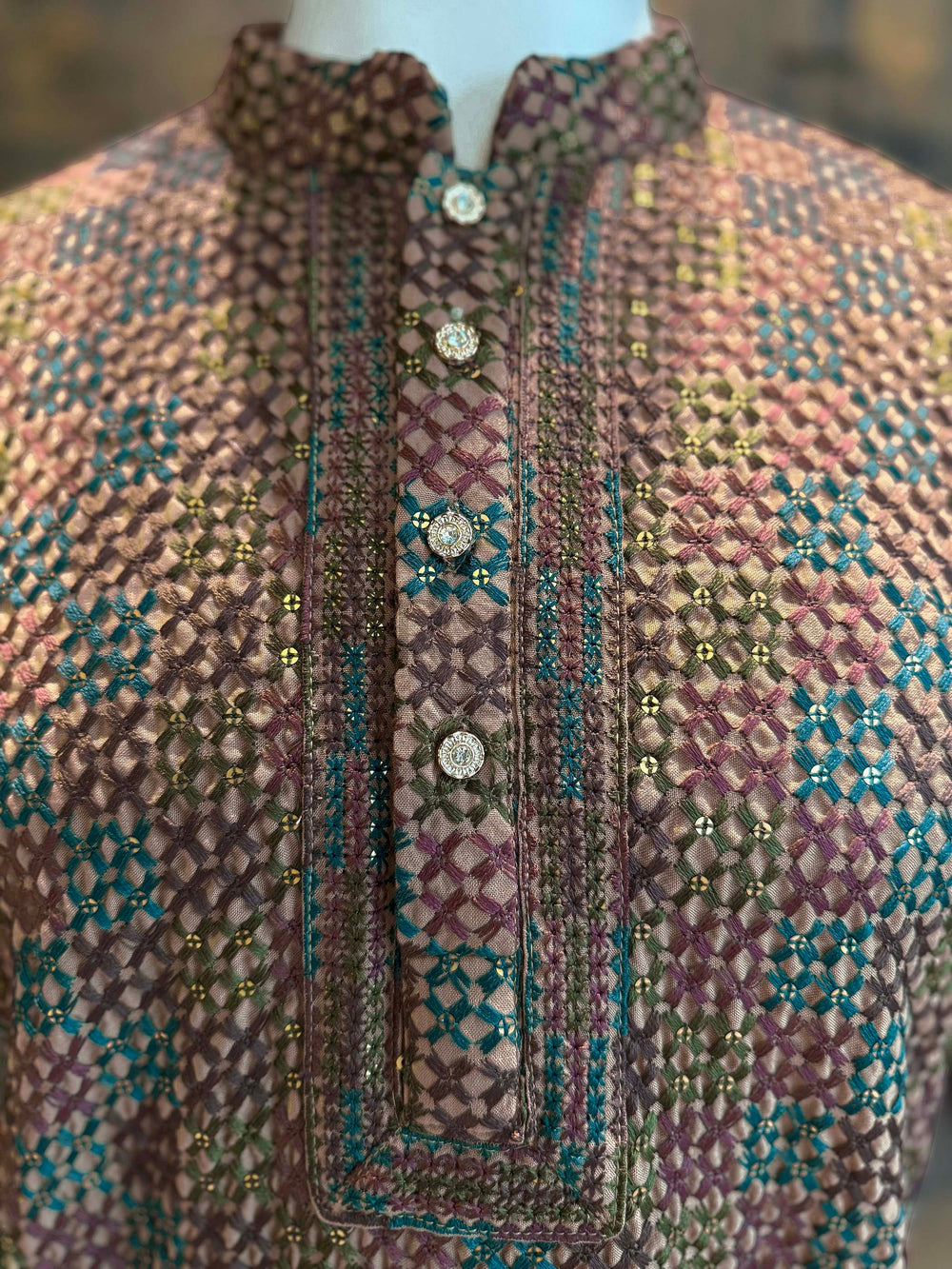 Close-up of a patterned garment with buttons on a mannequin. Close-up of mandarin collar kurta with ornate metallic buttons and intricate detailing.