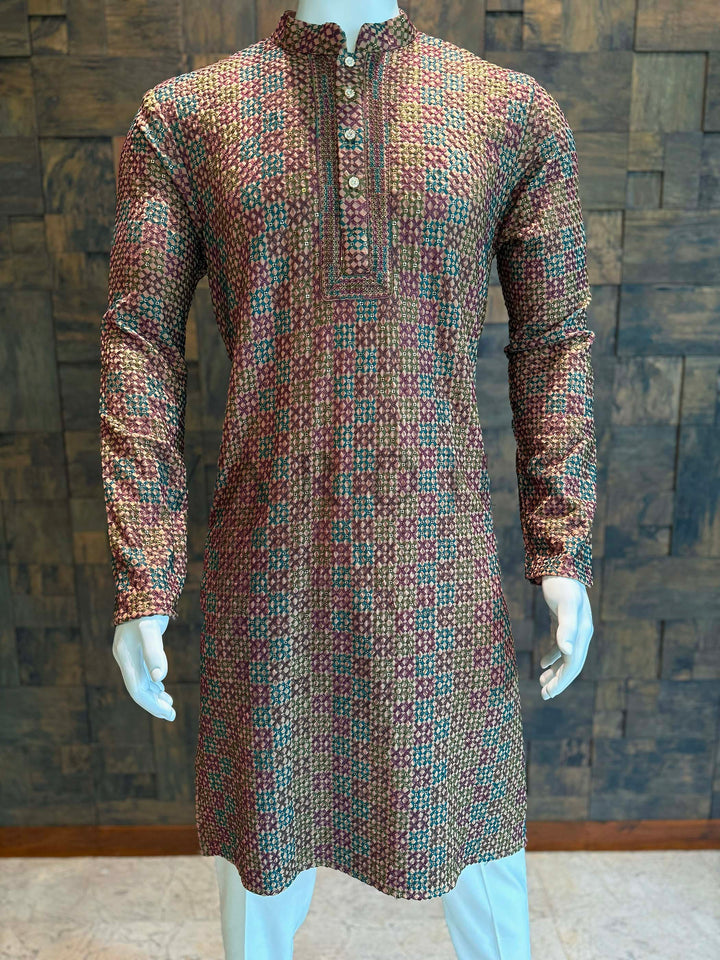 Patterned kurta on a mannequin against a textured wall background Designer kurta featuring golden thread highlights on a brown base with teal and maroon motifs.