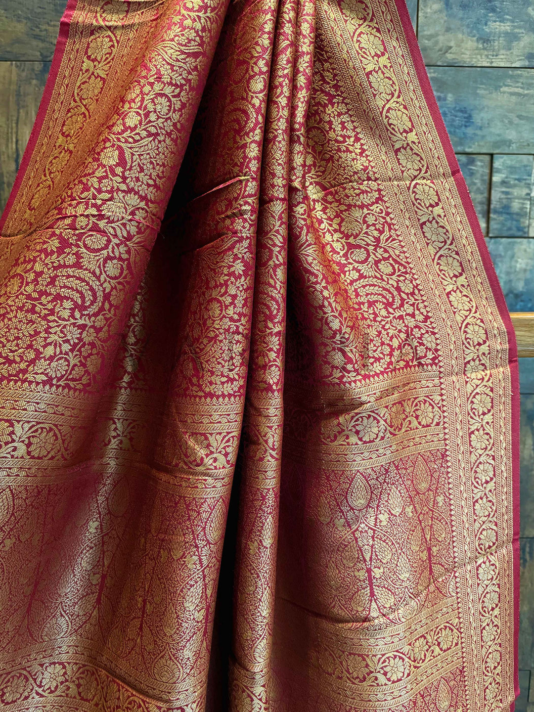 Close-up of a maroon saree with gold and red patterns against a wooden background. Pallu close-up highlighting the symmetrical jaal and traditional design layout Draped mannequin view of the saree showcasing contrast blouse and gold zari reflections in natural lighting