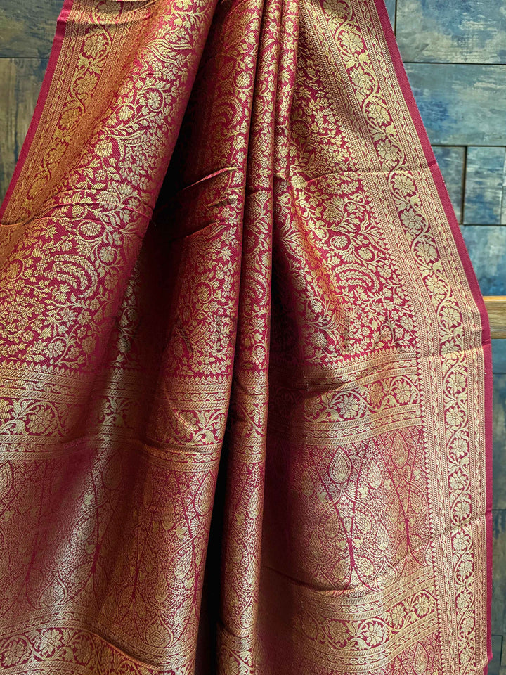 Close-up of a maroon saree with gold and red patterns against a wooden background. Pallu close-up highlighting the symmetrical jaal and traditional design layout Draped mannequin view of the saree showcasing contrast blouse and gold zari reflections in natural lighting