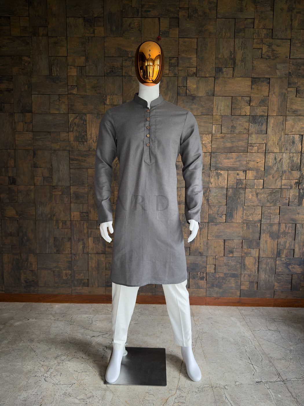 Mannequin wearing a gray kurta with white pants against a wooden paneled wall. Front view of a man wearing a House of Vardha slate grey micro-textured cotton kurta. Elegant men's ethnic wear perfect for festive parties, pujas, and smart-casual traditional events.