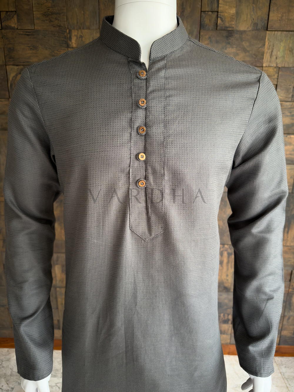 Gray kurta with brown buttons on a mannequin against a wooden paneled wall. Detailed chest view highlighting the crisp mandarin collar and contrast buttons on the premium grey textured cotton designer kurta for men.