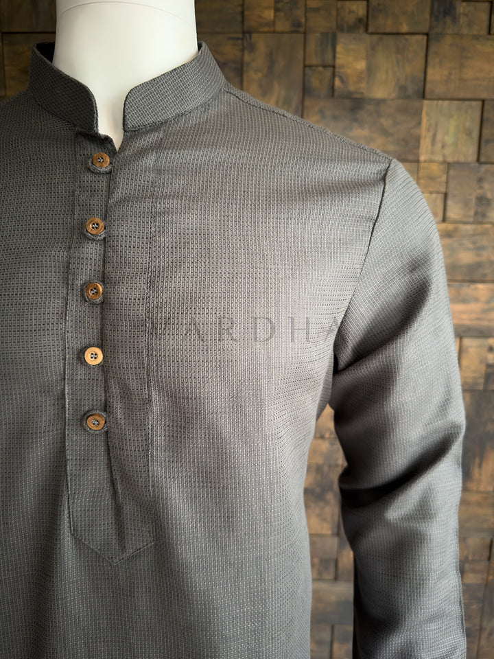 Gray kurta with brown buttons on a mannequin against a wooden paneled wall. Side angle of the tailored grey cotton kurta for men, emphasizing the structured fit and subtle woven texture, ideal for sophisticated evening and day wear.