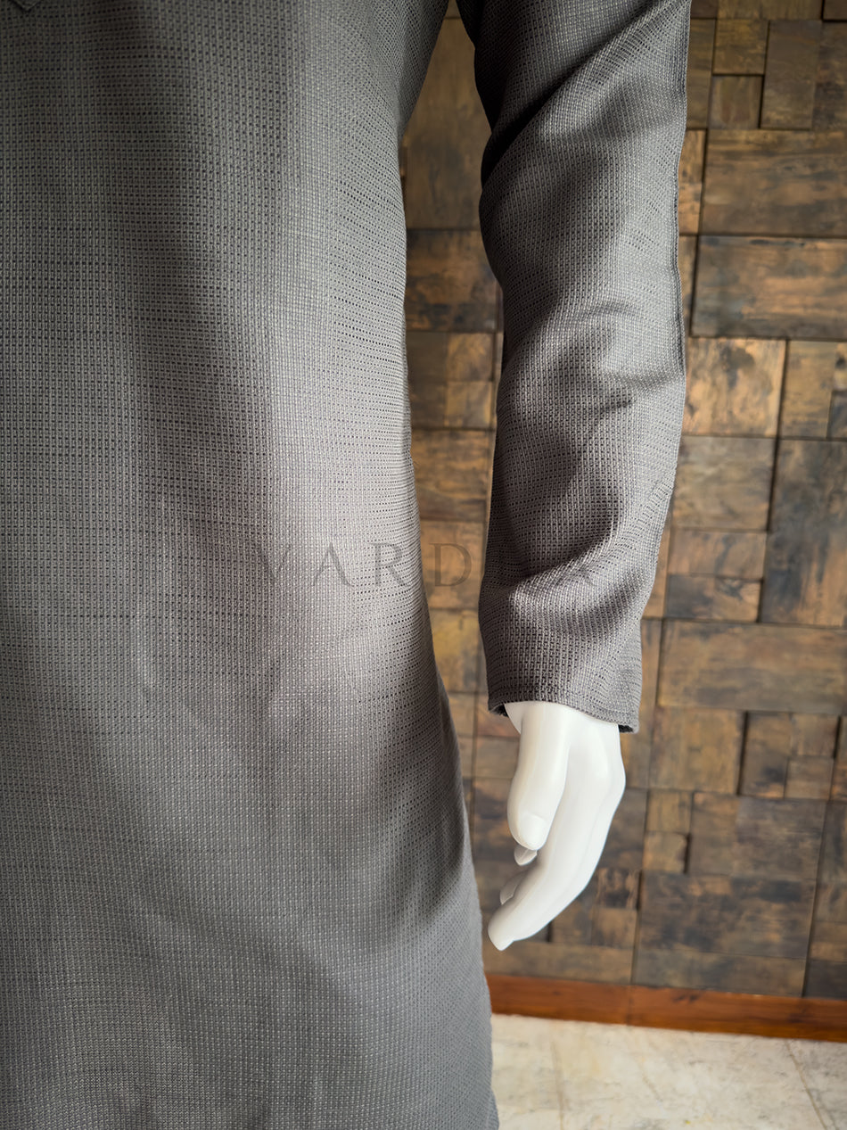 Gray textured coat on a mannequin against a wooden paneled wall. Close-up of the full sleeve and side drape of the slate grey textured cotton kurta, showcasing the breathable premium fabric and clean, minimalist aesthetic.