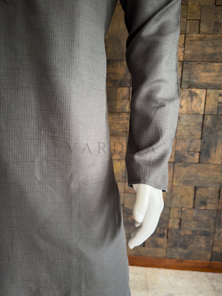 Gray textured coat on a mannequin against a wooden paneled wall. Close-up of the full sleeve and side drape of the slate grey textured cotton kurta, showcasing the breathable premium fabric and clean, minimalist aesthetic.