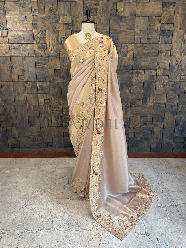 Full-length view of an elegant champagne gold tissue silk designer saree draped on a mannequin, featuring a broad golden border with intricate peacock and floral embroidery. Perfect for Indian weddings and festive ethnic wear.