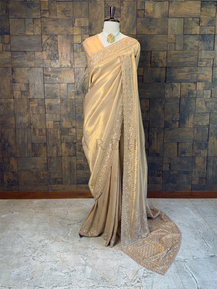 Chikoo saree with intricate patterns on a mannequin against a textured wall. Full View Chikoo Gold Viscose Saree with Cutdana Handwork, available with pre-drape services and free gift services.
