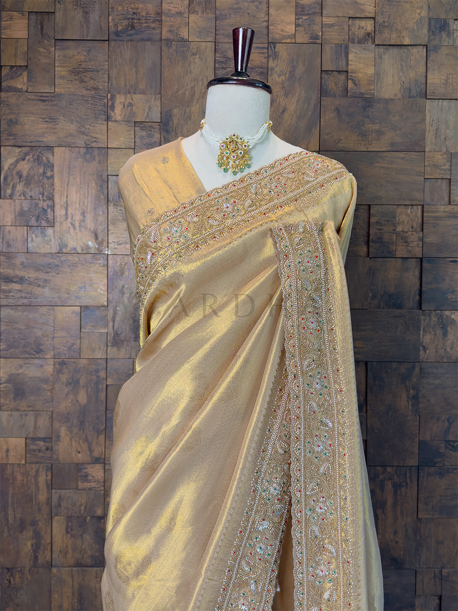 Chikoo saree with intricate embroidery on a mannequin against a wooden paneled wall. Designer Heavily Embroidered Scalloped Border on Chikoo Bronze Saree, complete with fall and edging.