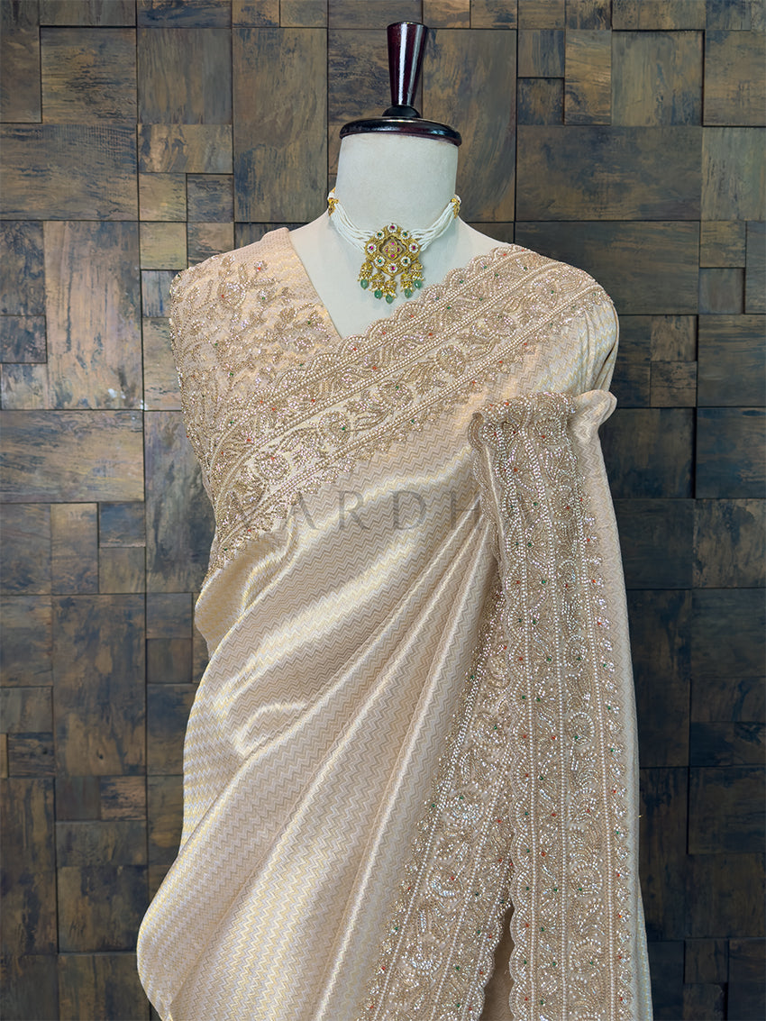 Cream saree with intricate patterns on a mannequin against a textured wall. Close Up of Woven Chevron Pattern and Scalloped Zircon Border on Bronze Beige Fabric, complete with fall and edging.