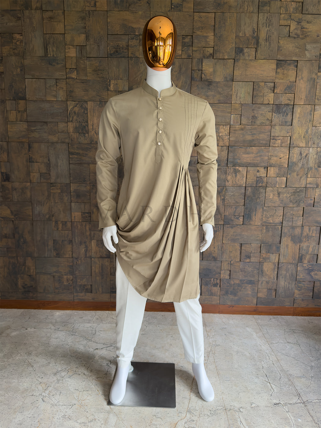 Mannequin wearing a beige kurta with a draped design against a wooden paneled wall. Front view of a man wearing a House of Vardha chiku beige cotton kurta featuring an asymmetric cowl drape and pintuck pleats. Perfect men's ethnic wear for modern weddings and festive parties.
