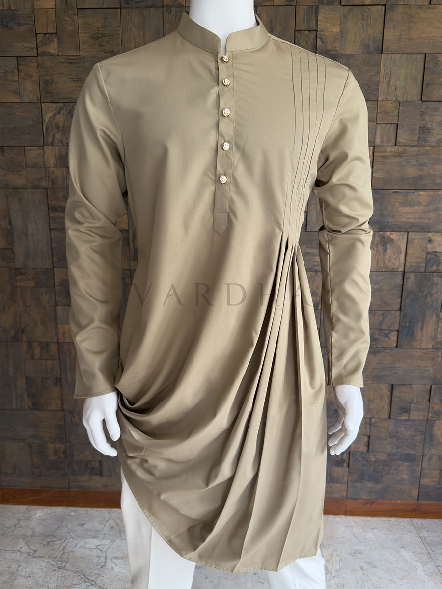 Beige kurta on a mannequin against a wooden paneled wall. Close-up of the light khaki men's festive kurta showcasing the unique side pleating that falls into a dramatic swooping drape. Premium tailored menswear for grand receptions.