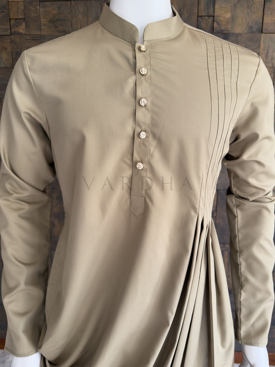 Beige kurta on a mannequin against a wooden background. Detailed chest view of the jeweled decorative buttons and the sharp pintuck pleats on the right shoulder of the chiku beige designer kurta for men.
