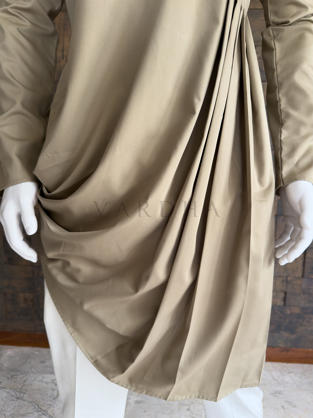 Beige fabric draped over a mannequin with white gloves, on a neutral background. Close-up of the full sleeve and the voluminous side folds of the asymmetric drape on the chiku beige cotton kurta, offering a contemporary twist on traditional wear.