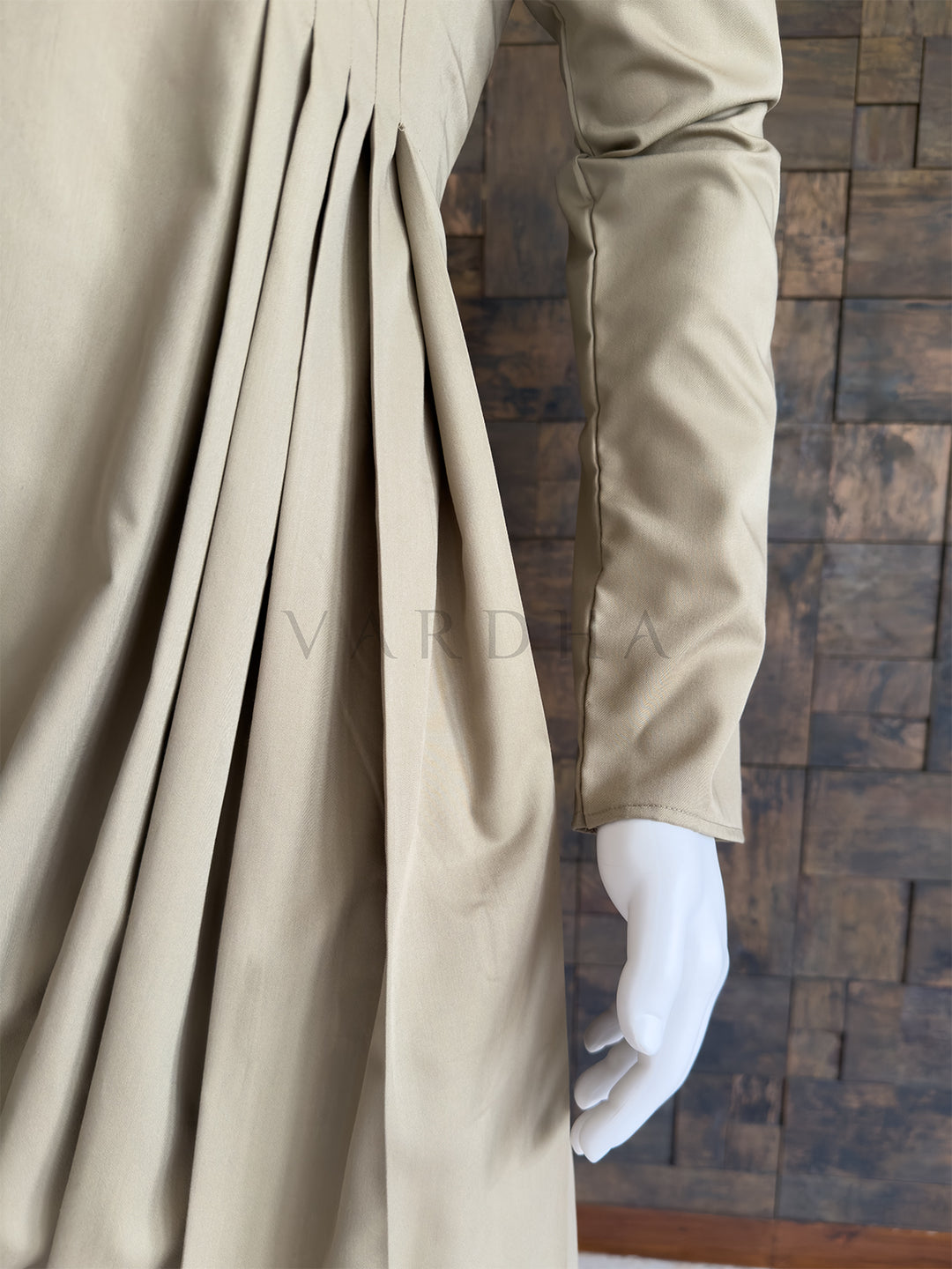 Beige fabric with a textured background. Detailed view of the sweeping cowl hemline and structural pleats on the elegant beige cotton designer kurta, paired with light trousers for special occasions.