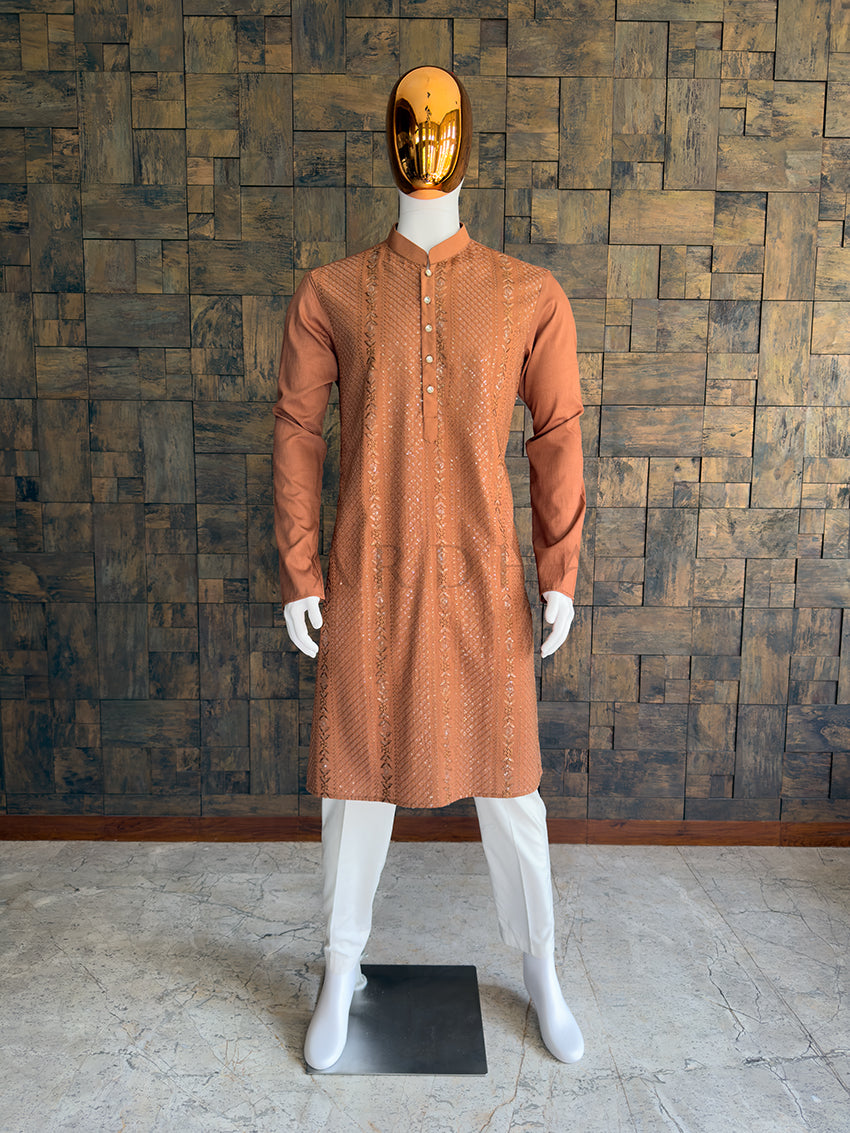Mannequin wearing a brown kurta with white pants against a wooden paneled wall. Front view of a man wearing a House of Vardha coffee brown viscose kurta featuring diagonal sequin embroidery and vertical floral motifs. Perfect men's ethnic wear for evening weddings, receptions, and festive celebrations.