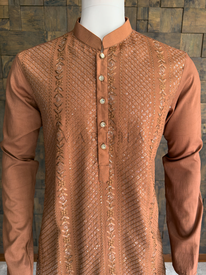 Brown embroidered kurta on a mannequin against a wooden paneled wall. Detailed chest view highlighting the premium rhinestone buttons and the rich copper-brown sequin embroidery on the luxurious viscose designer kurta for men.