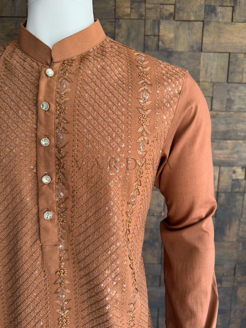 Brown embroidered shirt on a mannequin against a wooden paneled wall. Close-up of the solid coffee brown full sleeve contrasting with the heavily embroidered bodice, showcasing the tailored drape and premium quality of the festive menswear.