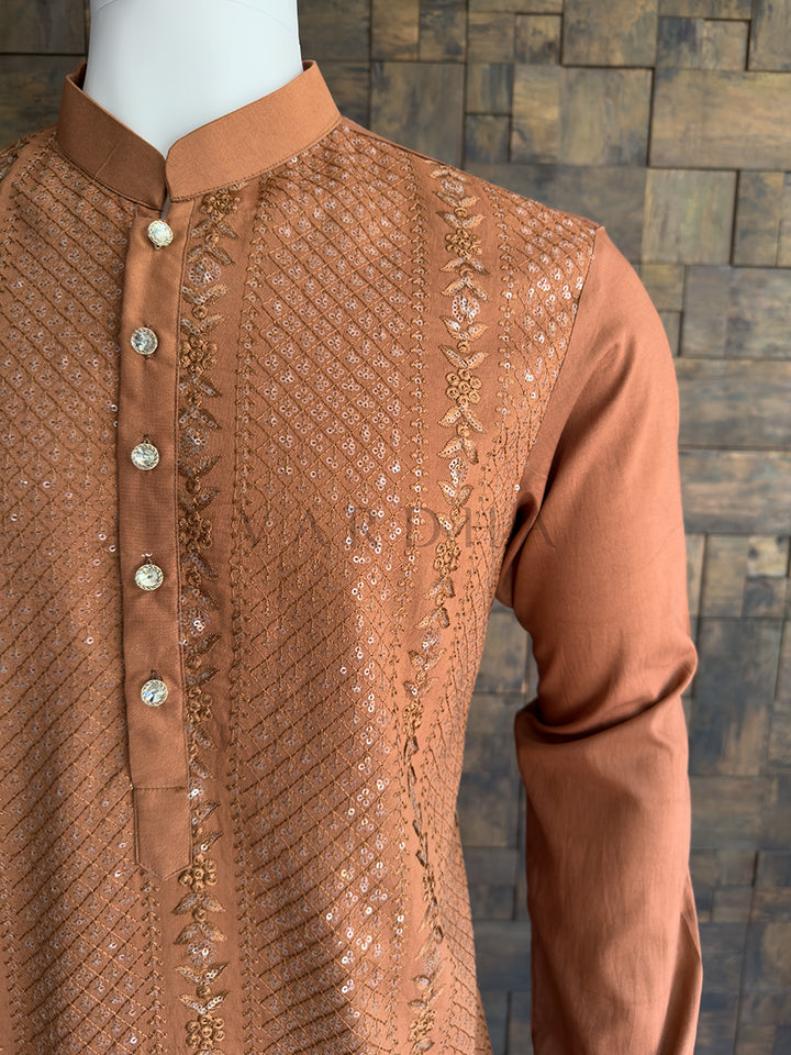 Brown embroidered shirt on a mannequin against a wooden paneled wall. Close-up of the solid coffee brown full sleeve contrasting with the heavily embroidered bodice, showcasing the tailored drape and premium quality of the festive menswear.