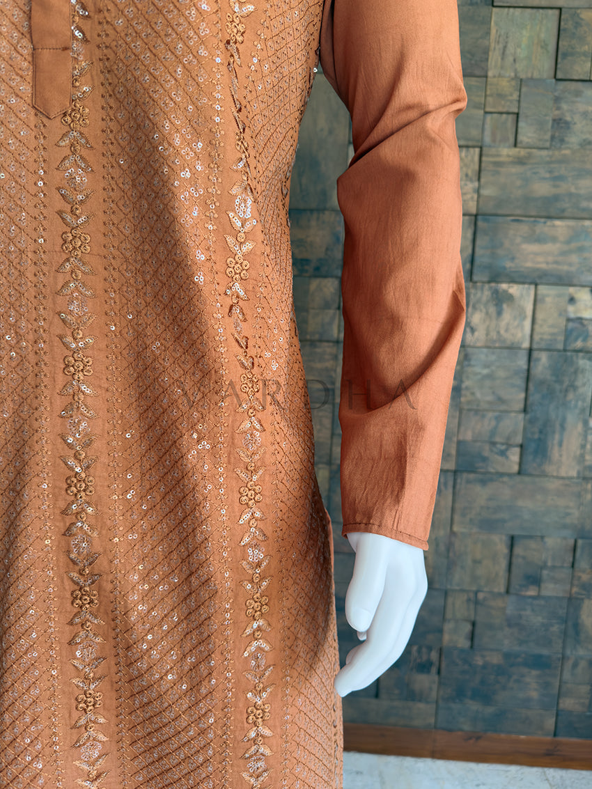 Brown embroidered garment on a mannequin against a wooden paneled wall. Full-length view of the striking coffee brown designer kurta paired with white pyjama bottoms, highlighting the sophisticated silhouette for sangeet and wedding wear.