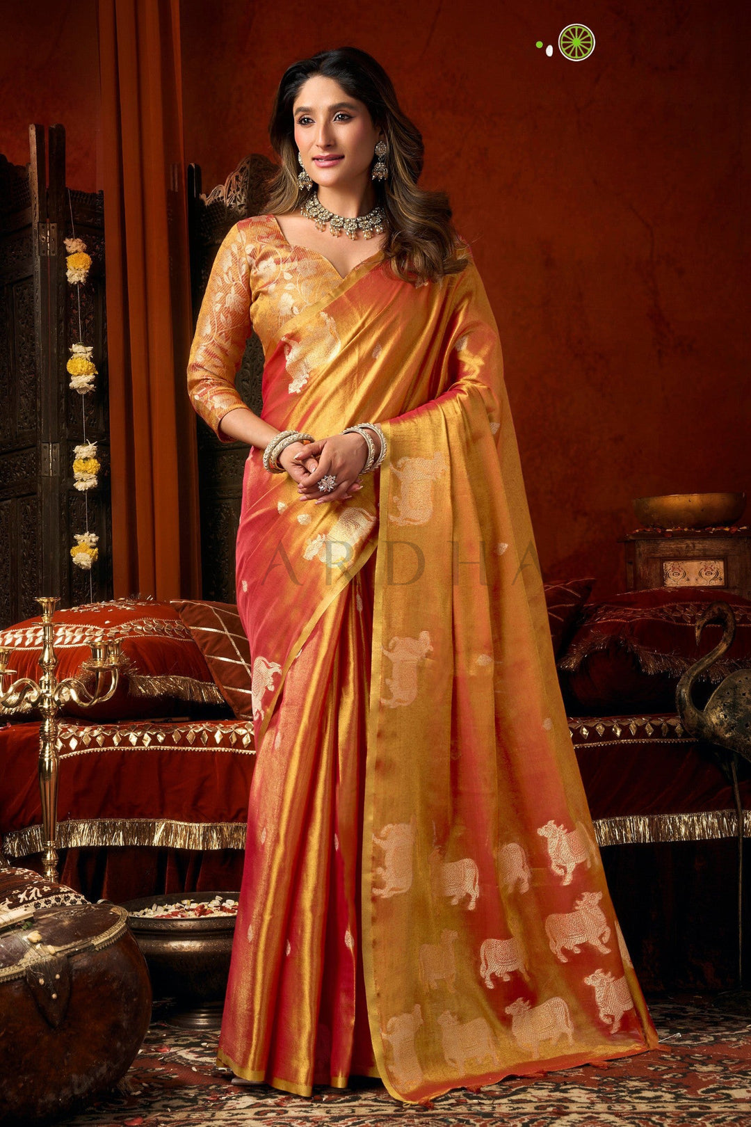 Woman in a traditional saree with a rich background Full front view of a dual-tone coral red and gold heavy tissue saree featuring allover silver woven cow buttas and a rich golden zari border.