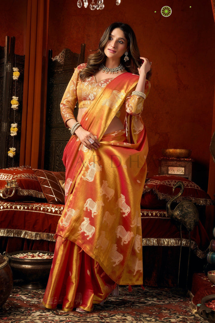 Woman in a traditional saree with a red and gold color scheme in an ornate room. Stylish front drape of the red and gold heavy tissue silk saree showcasing its luxurious texture, perfect for wedding wear and grand pujas.