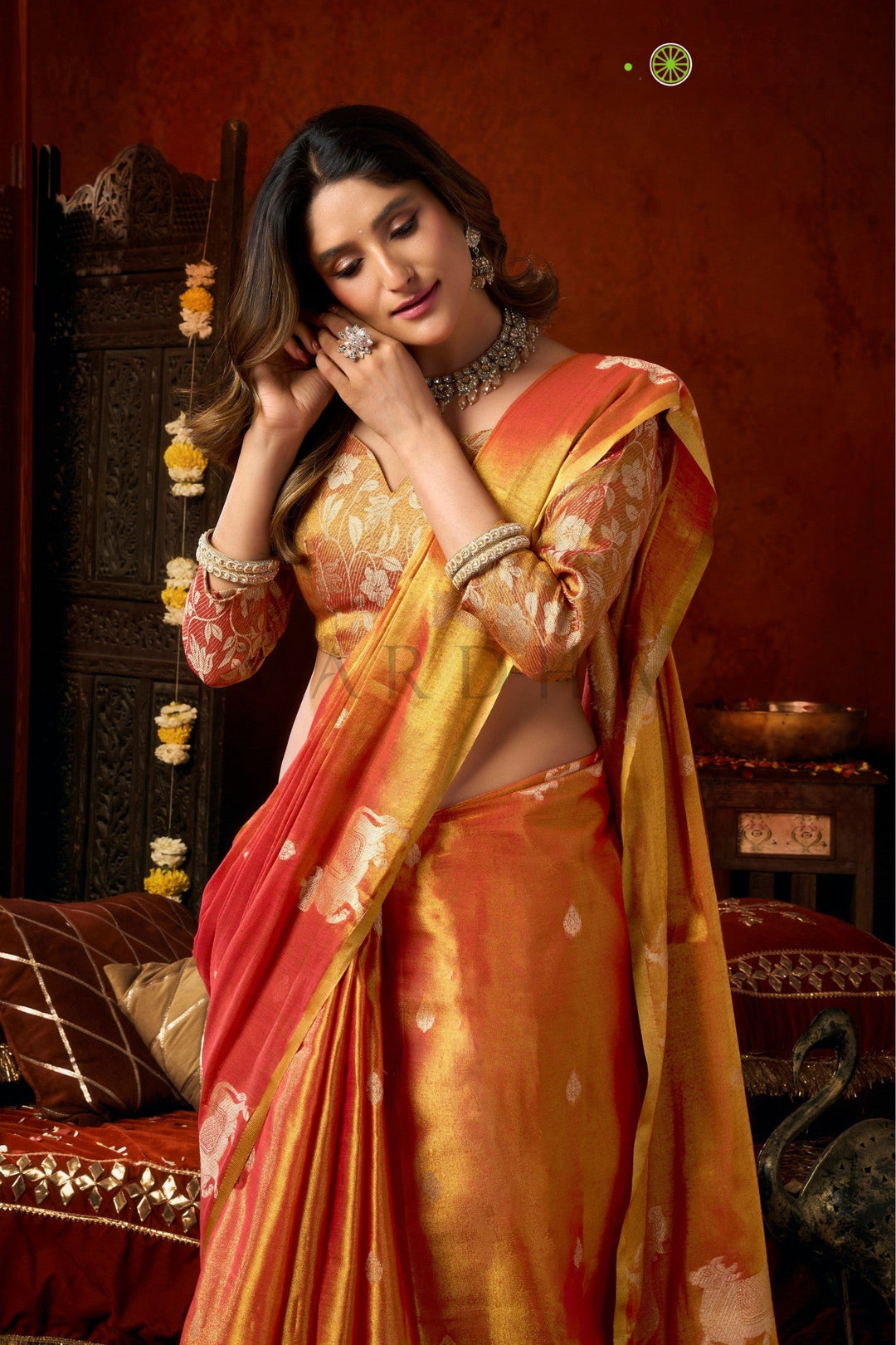Woman in a traditional orange and pink saree with jewelry against a warm-toned background Close-up of the tissue silk saree pallu showcasing traditional woven cow motifs on a vibrant red and gold base.