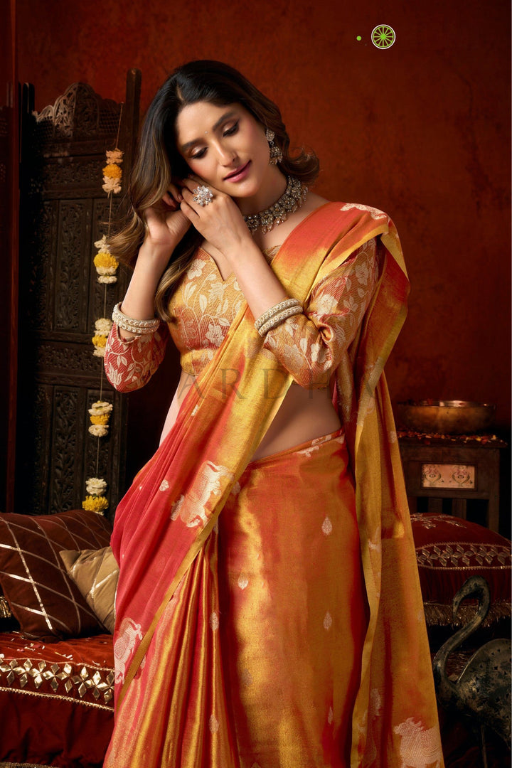 Woman in a traditional orange and pink saree with jewelry against a warm-toned background Close-up of the tissue silk saree pallu showcasing traditional woven cow motifs on a vibrant red and gold base.