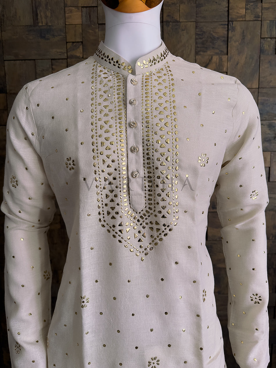Beige embroidered kurta on a mannequin against a wooden paneled wall. Traditional cream cotton kurta with gold mukaish detailing perfect for wedding and festive occasions