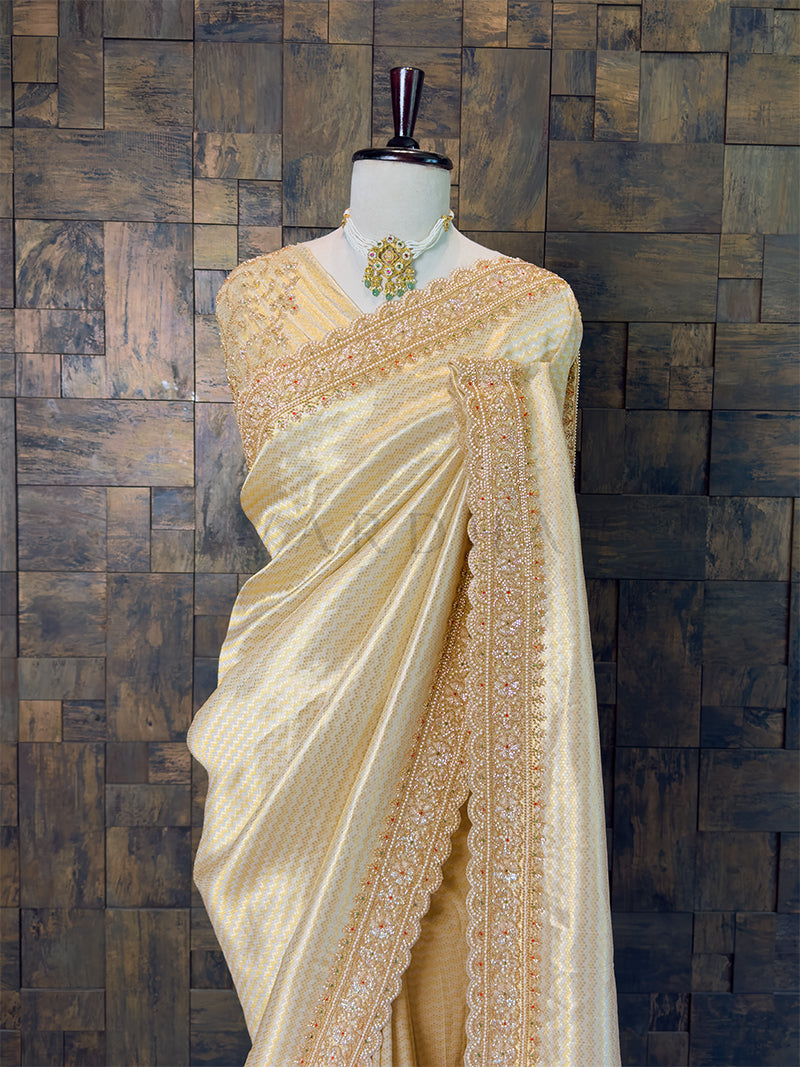 Cream saree with gold embroidery on a mannequin against a wooden paneled wall. Designer Heavily Embroidered Pearl Blouse Piece paired with Ivory Saree