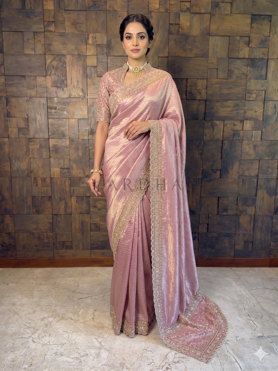Woman wearing a pink saree with a textured wall background