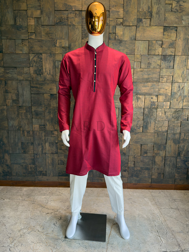 Mannequin wearing a red kurta with white pants against a wooden paneled wall. Men’s Crimson Red kurta crafted from premium cotton with a subtle woven slub texture, offering tactile depth and a slight festive sheen.
