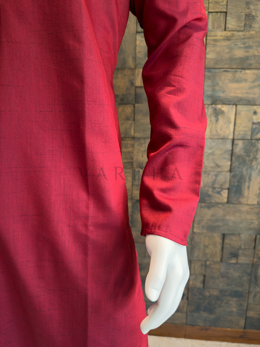 Red garment on a mannequin against a wooden paneled wall. Modern minimalist ethnic wear: A knee-length Crimson Red kurta with sharp black contrast detailing and clean, uninterrupted lines.