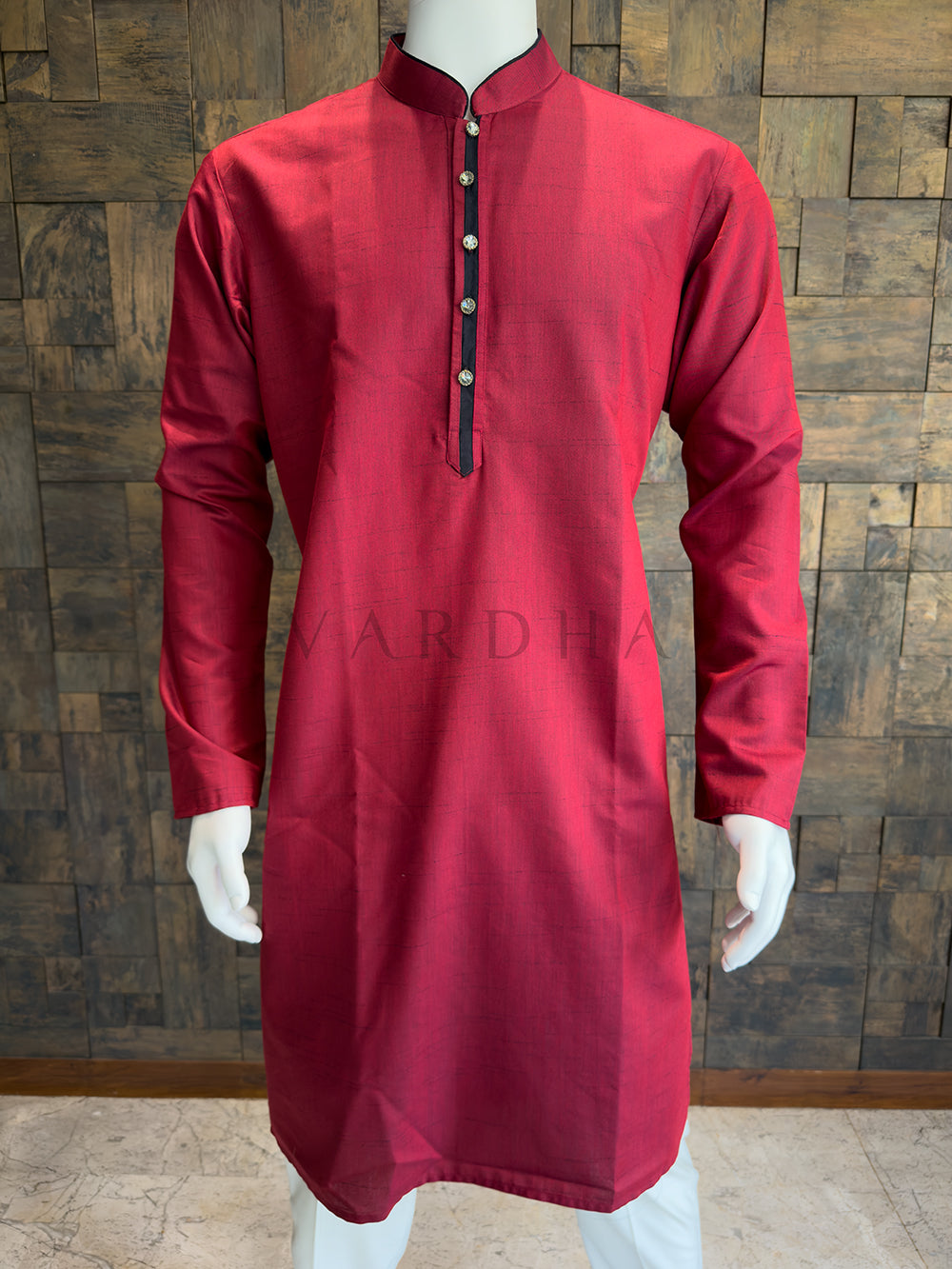 Red kurta on a mannequin against a wooden paneled wall. Premium breathable Crimson Red cotton kurta highlighting the rich slub weave and impeccable architectural tailoring for a polished festive appearance.