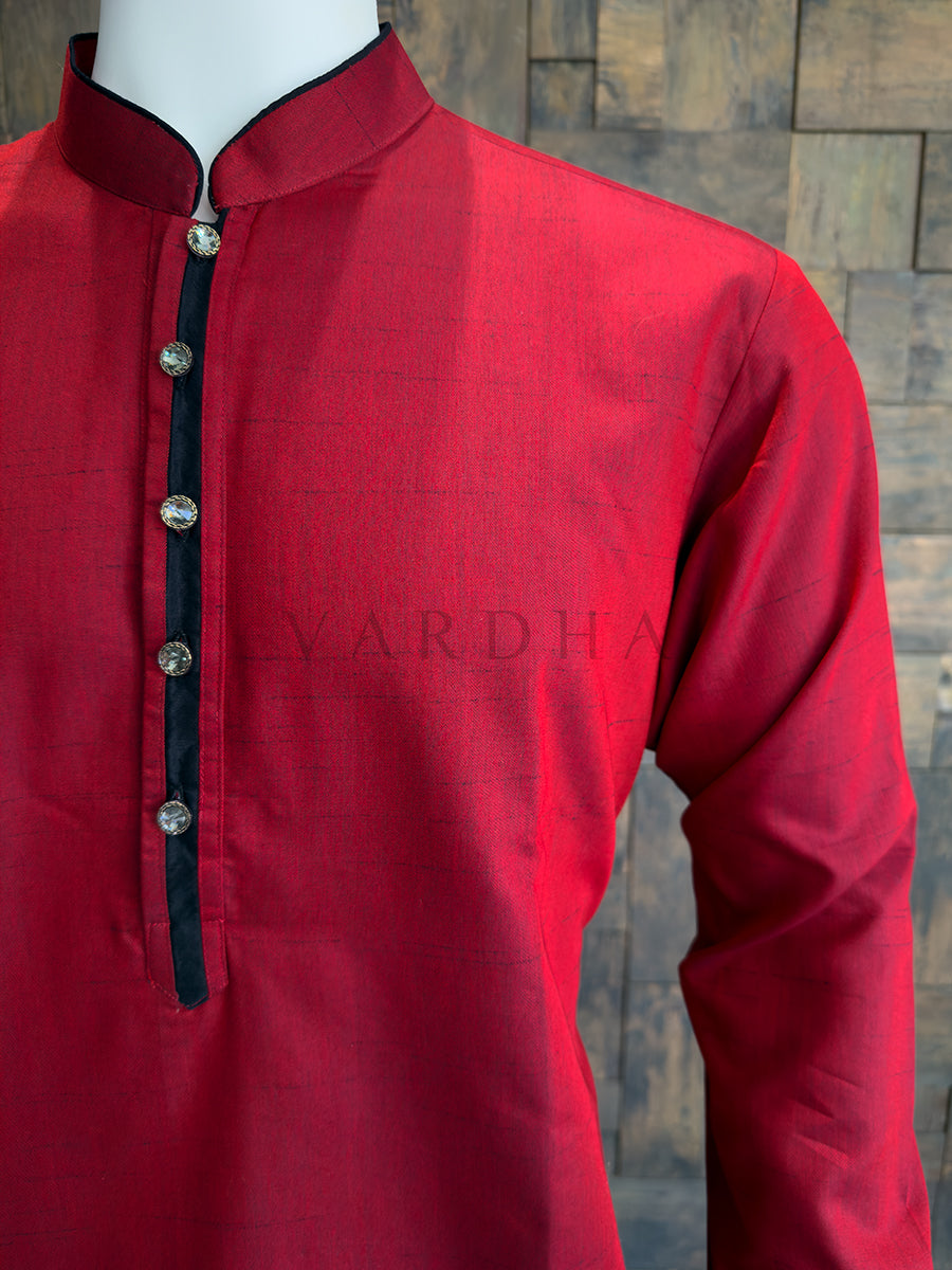Red kurta with black trim on a mannequin against a stone wall background. Sophisticated Crimson Red cotton kurta with black accents and metallic buttons; a bold ethnic essential that pairs perfectly with white or cream pyjamas.