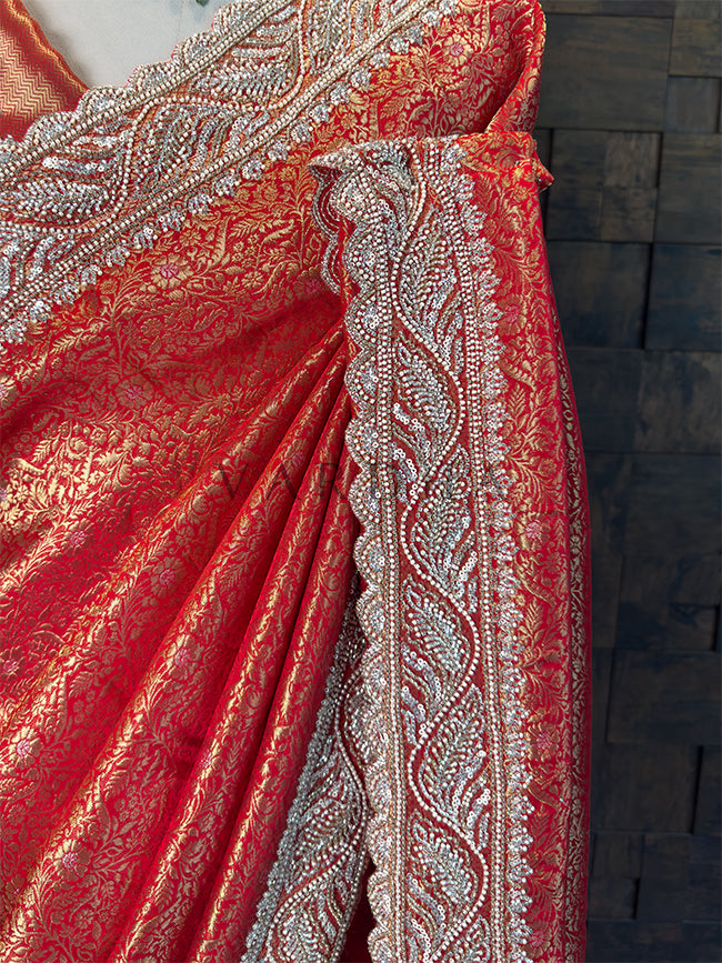 Close-up of a red fabric with intricate silver patterns on a wooden surface. Side Drape showing Structured Pleats and Cutdana Hand Embroidery on Kanjivaram Fabric