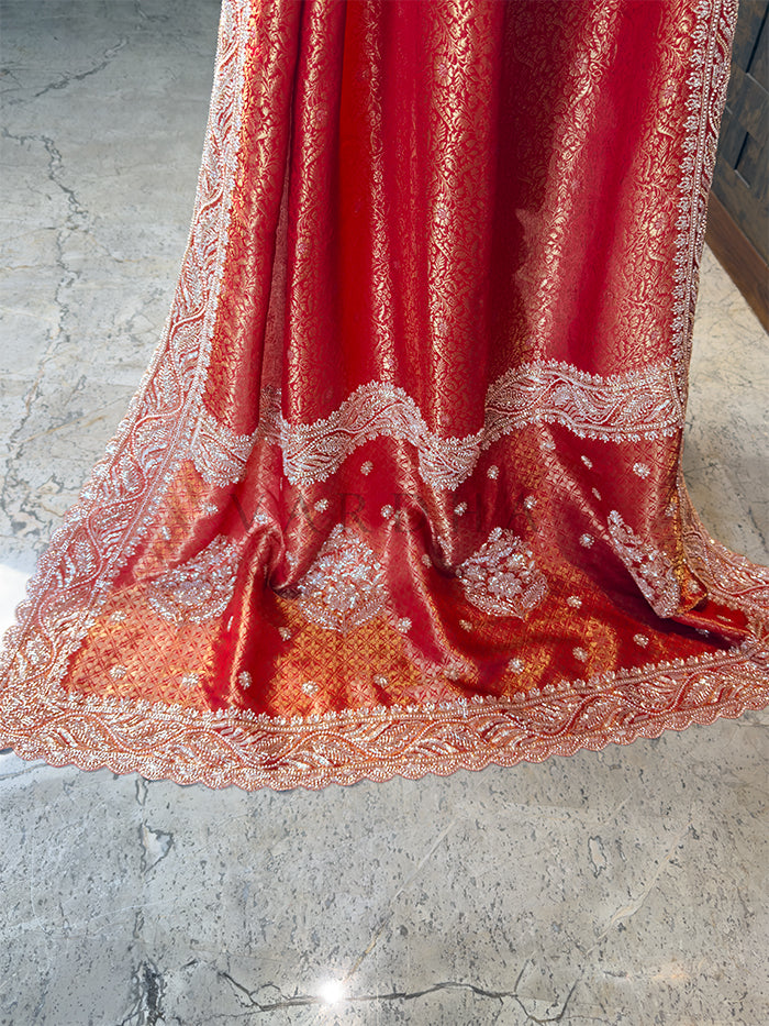 Red fabric with intricate white embroidery on a concrete floor. Close Up of Scalloped Zircon Stone Border on Crimson Red Silk Saree