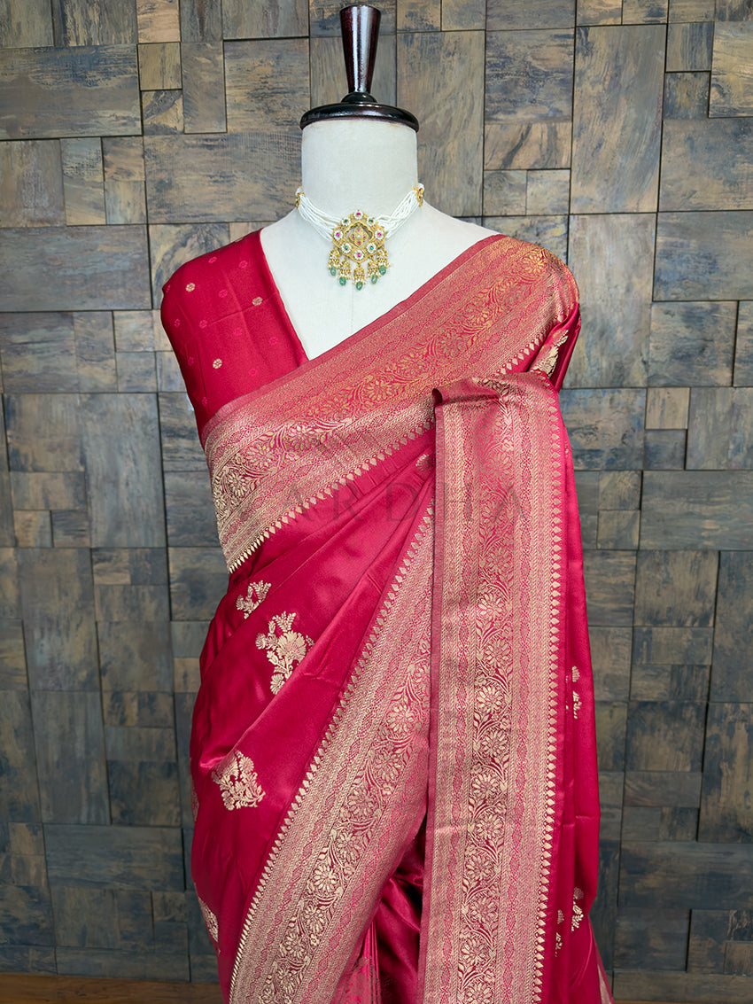 Red saree with gold embroidery on a mannequin against a wooden paneled wall. Lustrous Crimson Red Satin Saree by House of Vardha showcasing intricate Light Gold Zari weaving and a shiny, smooth texture. We offer Ready to wear, Pre drape service, Saree Add on, Custom Stitched Blouse, Fall and Edging, Gift Packaging at Complimentary Price!
